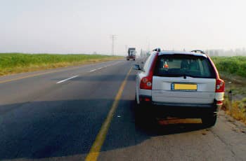 רכב פרטי עומד בשול הימני של כביש בין-עירוני, המסומן בקו צהוב רצוף. הרכב ממוקם כולו על השול, מימין לקו הצהוב, ורחוק ככל האפשר מנתיב הנסיעה.