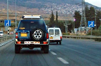 כביש עם שני נתיבים לאותו כיוון. משני צידי הכביש מוצבים תמרורים מלבניים כחולים זהים, המראים שהנתיב השמאלי מתמזג לתוך הנתיב הימני.