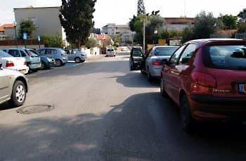 בתמונה נראה כביש עם מכוניות חונות משני צדדיו. באחת המכוניות החונות בצד ימין, הדלת האחורית השמאלית פתוחה לרווחה לתוך נתיב הנסיעה.