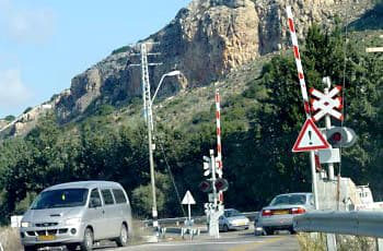 מפגש כביש עם מסילת ברזל, שבו המחסום האדום-לבן נמצא במצב מורם. ליד המחסום מוצבים שני תמרורים: תמרור בצורת X לבן, ומתחתיו תמרור אזהרה משולש עם סימן קריאה. הרמזור במפגש כבוי.