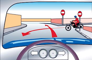 מבט מתוך רכב המתקרב לצומת T ומתכוון לפנות שמאלה, כפי שמסומן בחץ אדום. מימין מגיע רוכב אופנוע, ובכיוון נסיעתו מוצבים שני תמרורים עגולים אדומים עם פס לבן אופקי במרכזם.