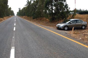 כביש בין-עירוני ישר עם נתיב אחד לכל כיוון. בצד ימין של הכביש, על שול עפר, עומד רכב פרטי במקביל לכביש.