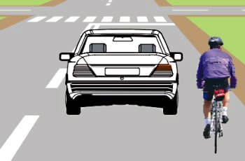 רכב נוסע בכביש ומתקרב לצומת. מימין לרכב, באותו נתיב ובאותו כיוון נסיעה, נוסע רוכב אופניים.