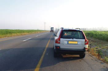 רכב פרטי חונה בשול הימני של כביש בין-עירוני. בנתיב הנסיעה שלצד הרכב החונה, נראית משאית נוסעת במרחק מה מלפנים.
