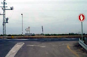 בתמונה נראה צומת T. בצד ימין של הכביש מוצב תמרור עצור, שהוא מתומן אדום עם כף יד לבנה. על הכביש מסומן חץ לבן הפונה שמאלה, ולפני הכניסה לצומת מסומן קו עצירה.