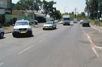 כביש עירוני עם שוליים בצד ימין. אבני השפה לאורך השוליים צבועות לסירוגין באדום ובלבן, ורכב חונה עליהם.