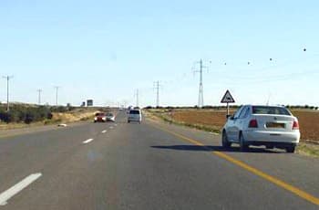 כביש בין-עירוני עם מספר נתיבים לאותו כיוון. רכב פרטי לבן עומד בשול הימני של הדרך, ולצידו מוצב תמרור אזהרה משולש המורה על פיתול ימינה.