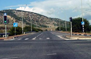 כביש רב-נתיבי עם רמזור המורה על אור ירוק. בהמשך הדרך, הנתיב הימני הולך וצר עד שהוא משתלב עם הנתיב השמאלי. משני צידי הכביש מוצבים תמרורים מרובעים כחולים עם חץ לבן, המורה על נסיעה ישר והתעקלות שמאלה.