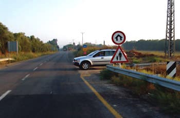 בצד ימין של הכביש מוצבים שני תמרורים, אחד מעל השני. התמרור העליון הוא עגול עם מסגרת אדומה, ובתוכו סמל של בית עם חץ הנכנס אליו. מתחתיו יש תמרור אזהרה משולש עם דמויות של מבוגר וילד. ליד התמרורים עומד רכב בשול הדרך.