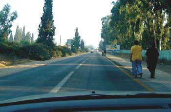 כביש בינעירוני עם פס הפרדה רצוף במרכזו. בשול הימני של הכביש הולכים מספר הולכי רגל, עם גבם לכיוון הנסיעה של הרכב המצלם.
