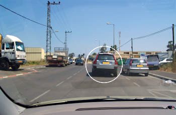 צילום מתוך רכב בנסיעה בכביש דו-סטרי עם נתיב אחד לכל כיוון, המופרד בקו מקווקו. בנתיב הנסיעה חונה רכב כסוף בחנייה כפולה וחוסם את הדרך. בנתיב הנגדי, מול הרכב, מתקרבת משאית.
