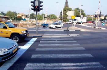 צומת עם רמזור המציג אור אדום. על הכביש, לפני מעבר החצייה, מסומן קו עצירה לבן ורציף.