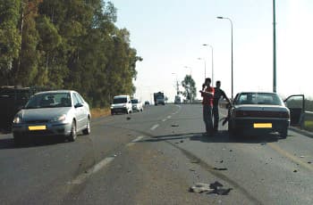 כביש עם מספר נתיבים בו רכב עצר בצד ימין. ליד הרכב עומדים שני אנשים על הכביש, ועל האספלט פזורים שברים וסימני בלימה.