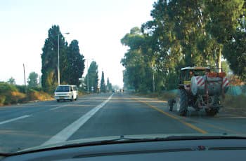 צילום מתוך רכב על כביש דו-סטרי. במרכז הכביש מסומן קו הפרדה רצוף לבן, המפריד בין נתיב הנסיעה לנתיב הנגדי. מימין לכביש יש שול עם קו צהוב רצוף, ועליו עומד טרקטור.