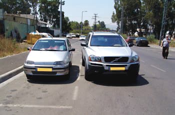 רכב אחד חונה במקום חניה מסומן בצד הדרך. רכב שני חונה במקביל אליו, בתוך נתיב הנסיעה.