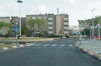 בתמונה נראה כביש המוביל לכיכר תנועה, ולפני הכיכר מסומן מעבר חצייה. בצד שמאל מוצבים שני תמרורים זה מעל זה: למעלה תמרור משולש הפוך של "תן זכות קדימה", ומתחתיו תמרור ריבוע כחול המציג הולך רגל על מעבר חצייה.