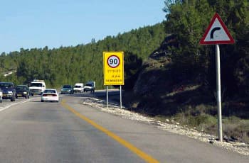 כביש דו-סטרי עם קו הפרדה רצוף, הנכנס לעיקול ימינה. בצד ימין מוצב תמרור אזהרה משולש המורה על עיקול חד ימינה. בצד שמאל מוצב תמרור מלבני צהוב עם המספר 90 בתוך עיגול אדום והכיתוב "סעו בזהירות".