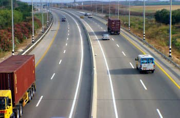 כביש מהיר רב-נתיבי עם גדר הפרדה מבטון בין שני כיווני הנסיעה. על הכביש נוסעים כלי רכב שונים, כולל מכוניות פרטיות ומשאיות, בנתיבים המסומנים בקווים מקווקוים.