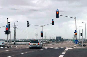 צומת מרומזר שבו הרמזורים בכיוון הנסיעה מראים אור אדום. מעל הרמזורים מוצבים תמרורים עגולים כחולים עם חצים לבנים המורים על כיווני הנסיעה המותרים מהנתיבים השונים.