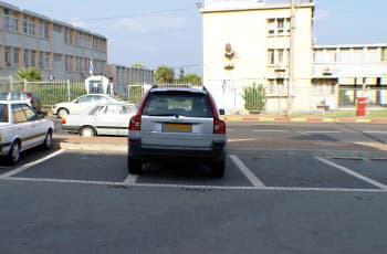 רכב חונה בתוך מקום חנייה המסומן בקווים לבנים על הכביש. ברקע נראית מדרכה הצבועה באדום-לבן.