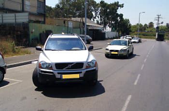 רכב כסוף עומד בזווית, כאשר חלקו בולט לתוך נתיב נסיעה פעיל. מאחוריו, באותו נתיב, מתקרבת מכונית נוספת.