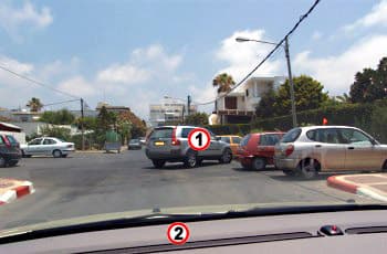 צילום מתוך רכב (2) המתקרב לרכב שטח כסוף (1). הרכב הכסוף יוצא בנסיעה לאחור מחנייה בצד ימין של הכביש וחוסם חלקית את נתיב הנסיעה.