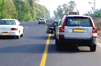 רכב חונה בשול הימני של כביש. דלת הרכב הפונה אל נתיב הנסיעה פתוחה, ואדם יוצא ממנו בזמן שבנתיב הסמוך נעה מכונית.